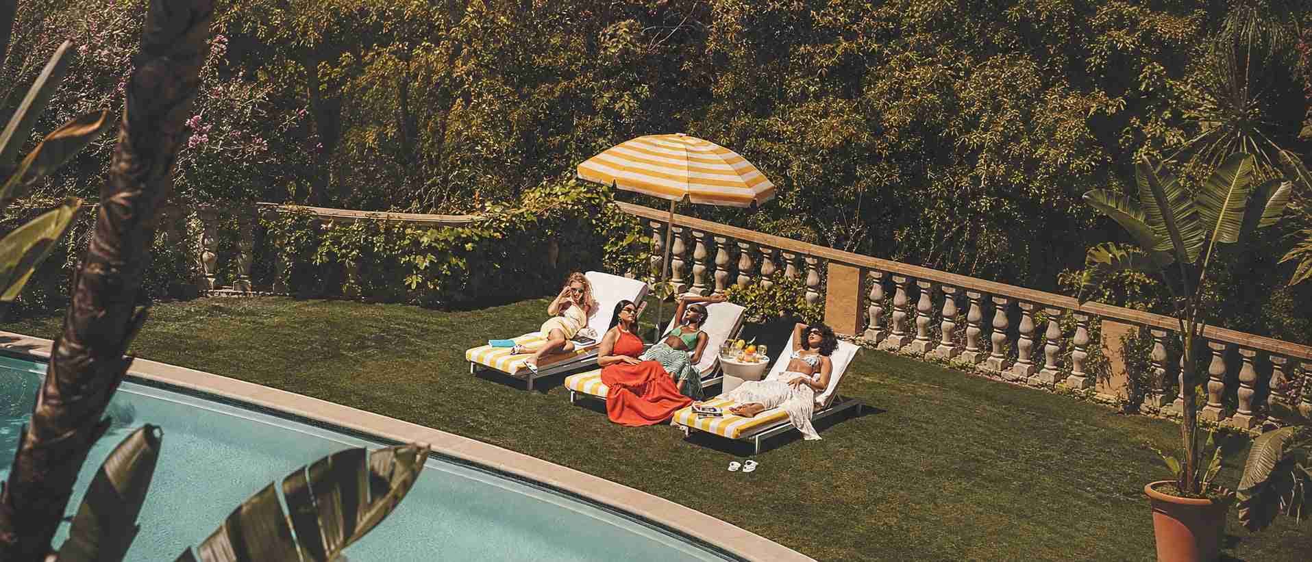 A sunlit pool terrace with striped parasols and loungers
